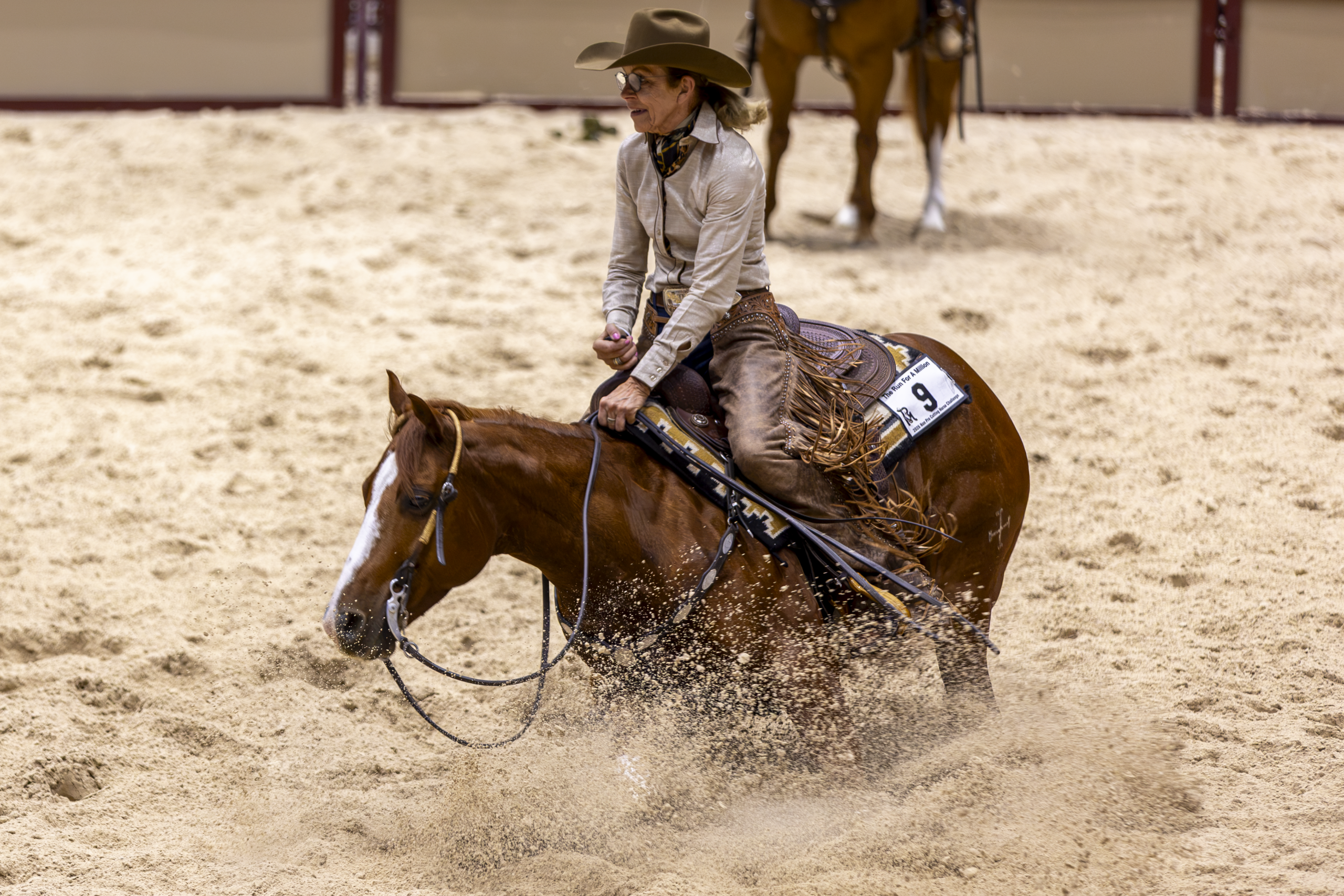 Barrel racer and horse kicking up dust while racing around a barrel in an arena