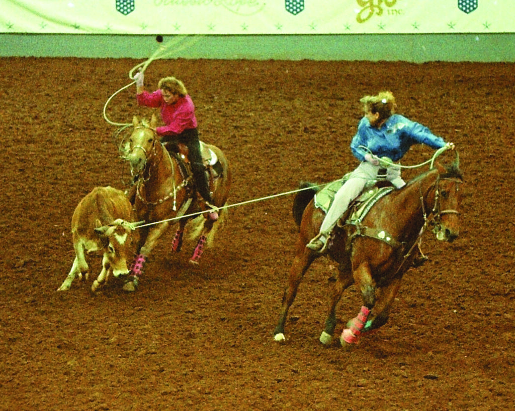 Two team ropers on horseback work a steer during competition in a dirt arena