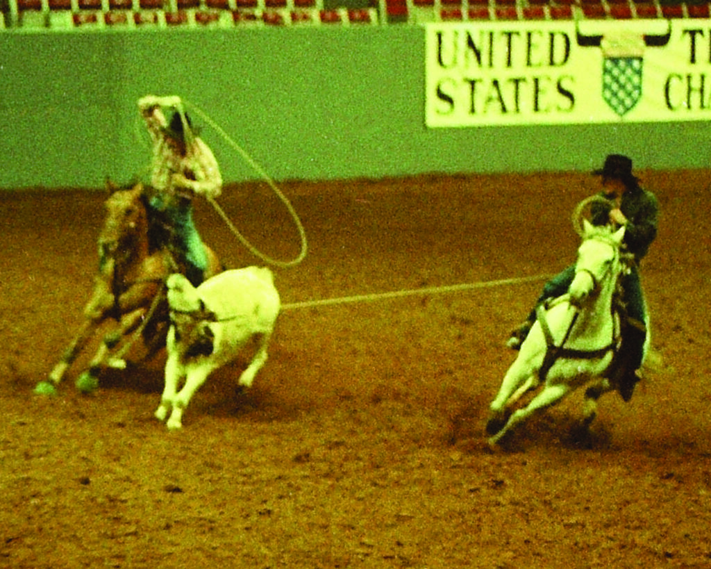 Team ropers on horseback work cattle in a dirt arena during a roping competition at the United States Team Roping Championships