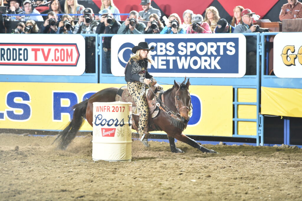 Barrel racer rounds a barrel marked "2017" at a rodeo with CBS Sports Network signage visible in the background