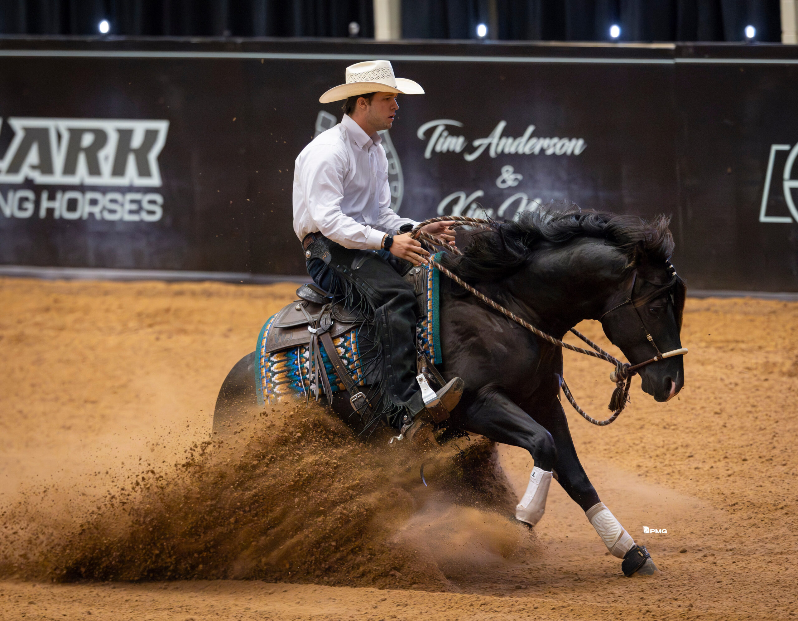 Reiner in white shirt and chaps slides his black horse to a dirt-spraying stop in an indoor arena